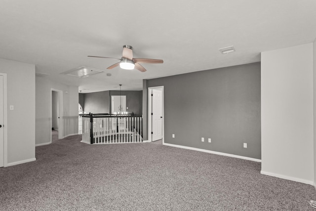 spare room with baseboards, carpet, attic access, and ceiling fan with notable chandelier