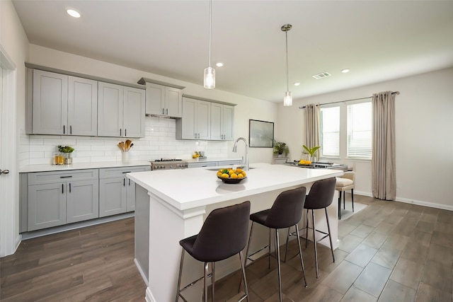 14238 Elkwood Pine Dr, Houston, TX 77032 - kitchen featuring an island with sink, a breakfast bar area, tasteful backsplash, a sink, and gray cabinetry