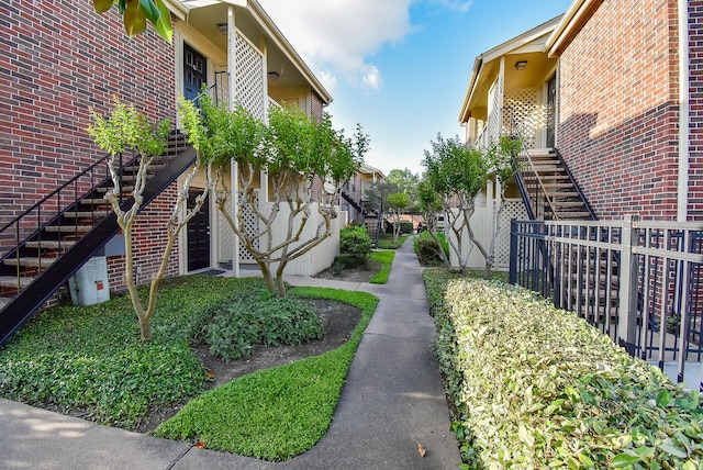 view of property exterior with brick siding, a residential view, fence, and stairway