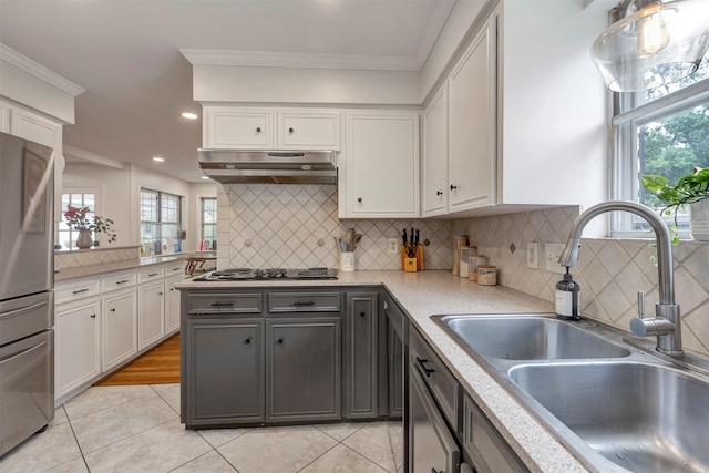 kitchen with a sink, light tile patterned floors, white cabinets, freestanding refrigerator, and under cabinet range hood