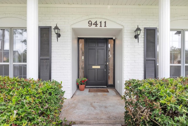 view of exterior entry featuring covered porch and brick siding