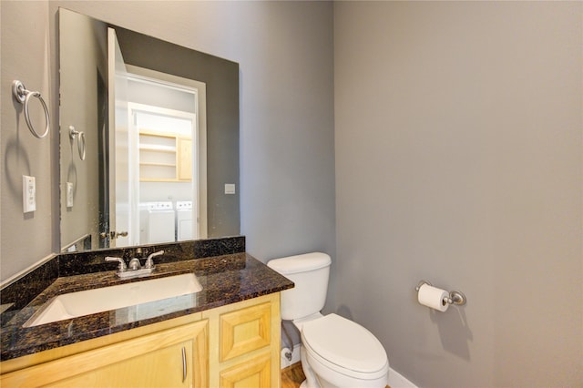 half bathroom featuring baseboards, vanity, toilet, and washing machine and clothes dryer
