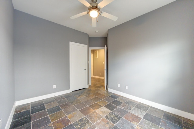 unfurnished room with baseboards, a ceiling fan, and stone tile floors