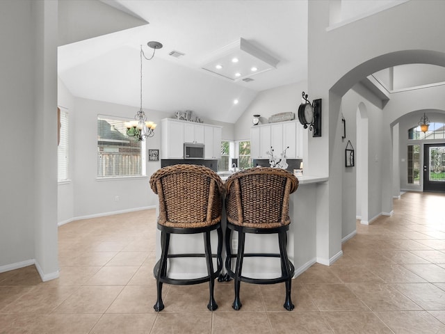 kitchen featuring a breakfast bar area, stainless steel microwave, white cabinets, arched walkways, and light tile patterned floors