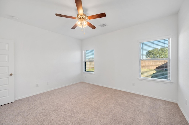 empty room featuring ceiling fan, visible vents, light carpet, and a wealth of natural light