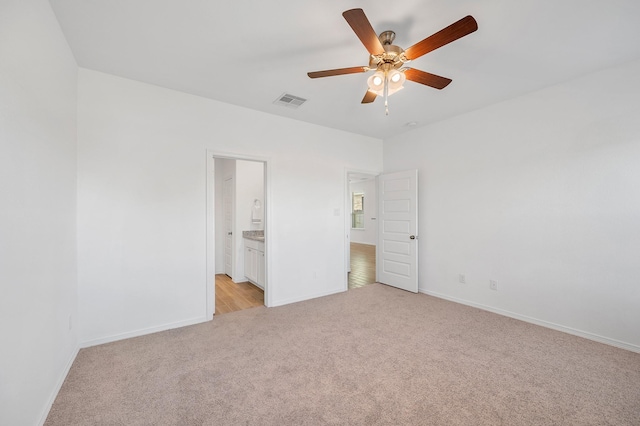 unfurnished bedroom with visible vents, baseboards, ensuite bathroom, light colored carpet, and a ceiling fan