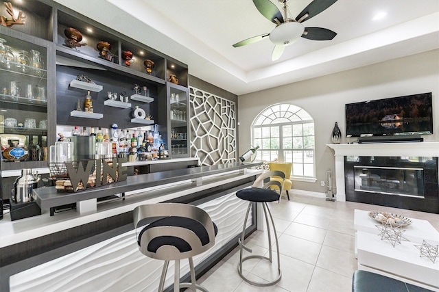 33519 Hillside Dr, Pinehurst, TX 77362 - indoor dry bar with a ceiling fan, tile patterned floors, baseboards, a glass covered fireplace, and a tray ceiling