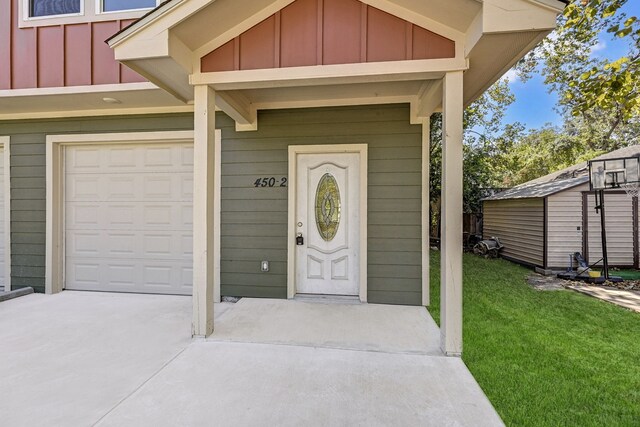 doorway to property featuring board and batten siding, a lawn, and concrete driveway