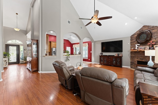living room with arched walkways, wood finished floors, and high vaulted ceiling