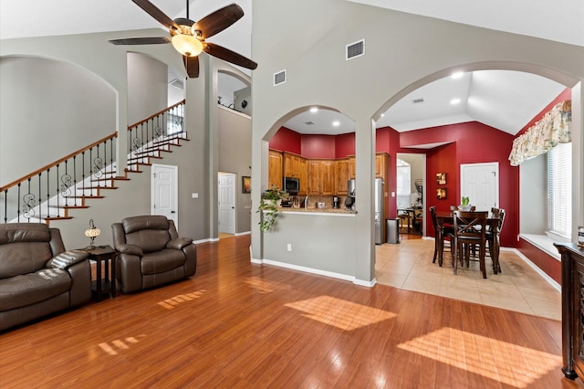 living area featuring a ceiling fan, high vaulted ceiling, visible vents, and light wood-type flooring