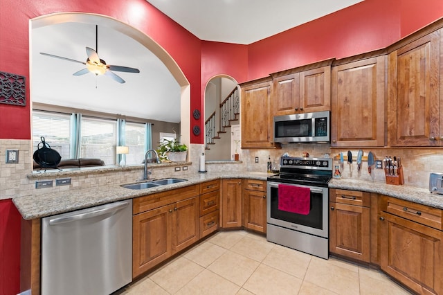 kitchen with brown cabinets, appliances with stainless steel finishes, a sink, a ceiling fan, and tasteful backsplash