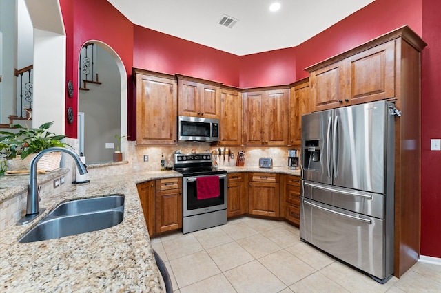 kitchen with visible vents, brown cabinetry, a sink, backsplash, and stainless steel appliances