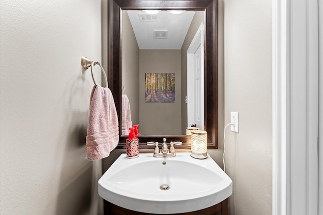 bathroom featuring a textured wall, visible vents, and a sink