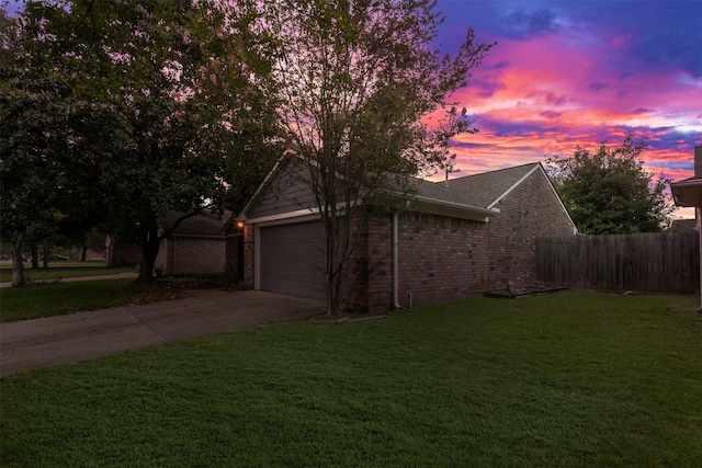 view of home's exterior with driveway, brick siding, fence, a yard, and an attached garage