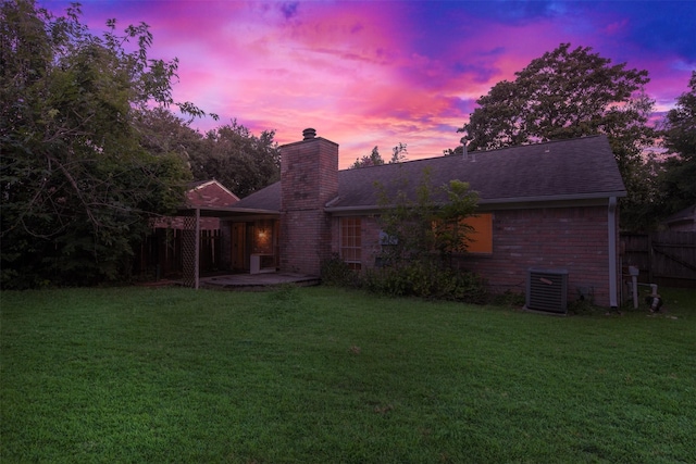 back of property at dusk with a chimney, a lawn, fence, a patio, and a shingled roof