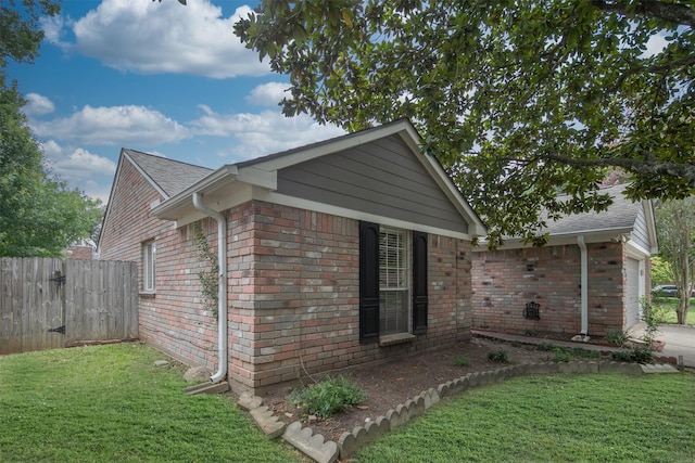 view of side of home with brick siding, fence, and a yard