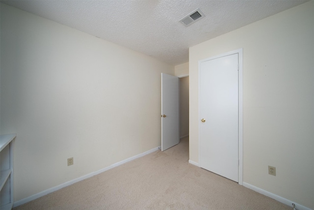 unfurnished bedroom featuring visible vents, a textured ceiling, baseboards, and light colored carpet