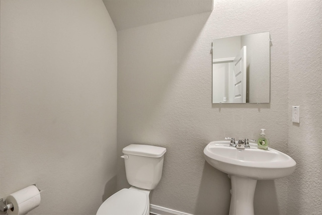 half bathroom with a sink, vaulted ceiling, and toilet