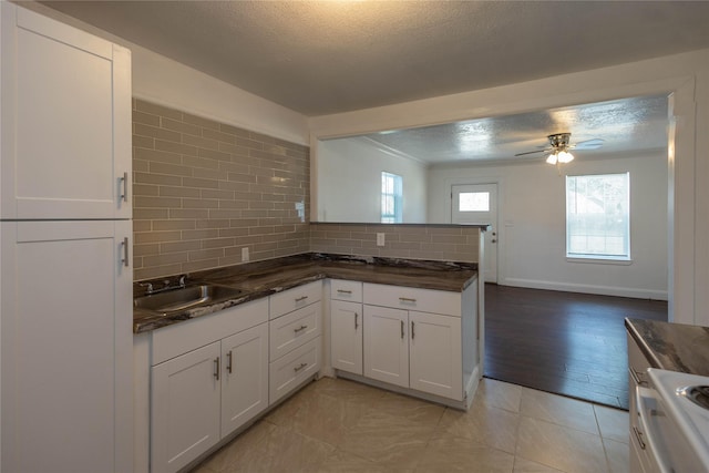 kitchen featuring white cabinets, a sink, a textured ceiling, a ceiling fan, and decorative backsplash