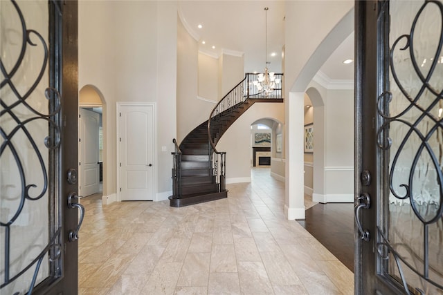 entryway with crown molding, a high ceiling, arched walkways, a chandelier, and stairs