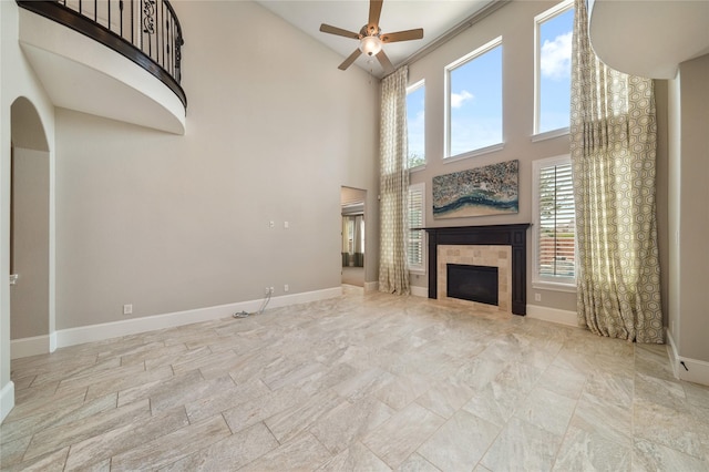 unfurnished living room with a ceiling fan, a high ceiling, a tiled fireplace, and baseboards