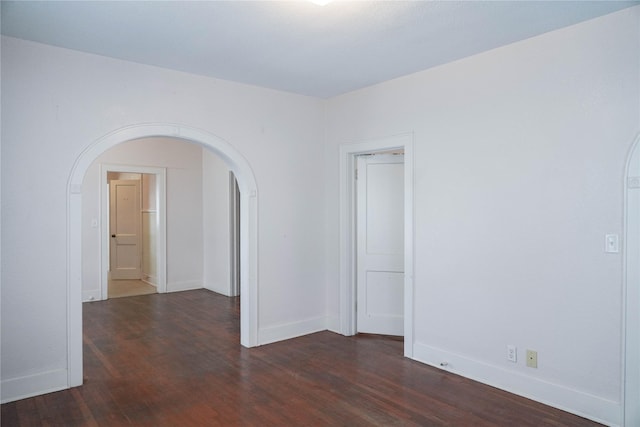 spare room with baseboards, arched walkways, and dark wood-style floors
