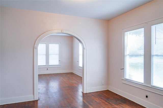 spare room featuring dark wood-style flooring, arched walkways, and plenty of natural light