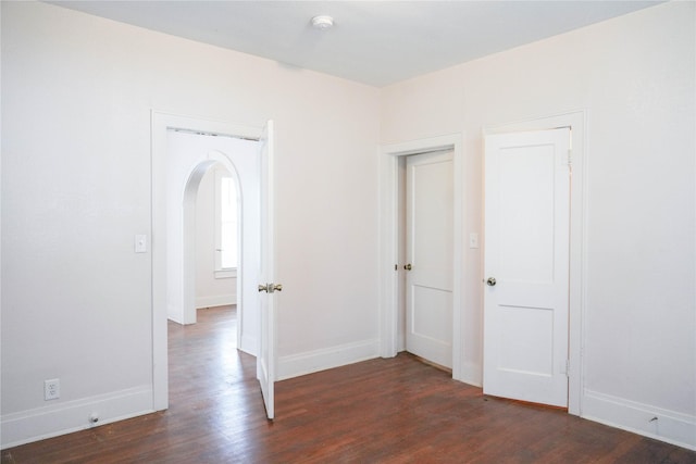 unfurnished room with arched walkways, baseboards, and dark wood-style floors