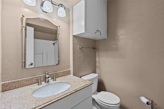 bathroom featuring toilet, a textured wall, and vanity