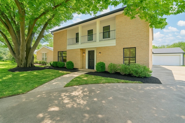 traditional-style home featuring a detached garage, brick siding, a balcony, and a front yard