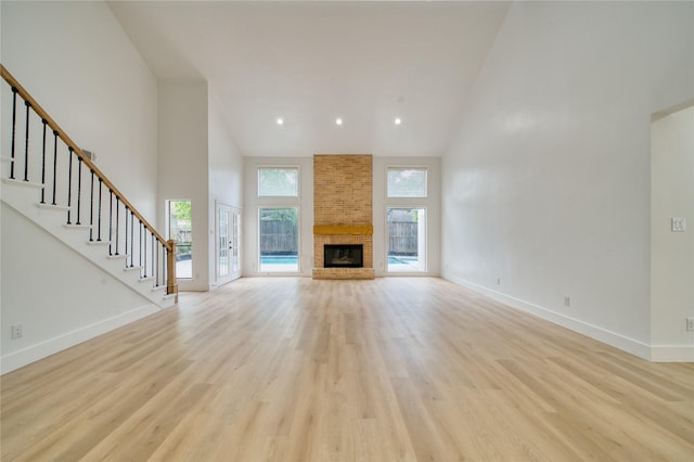 unfurnished living room with high vaulted ceiling, baseboards, and light wood-style flooring