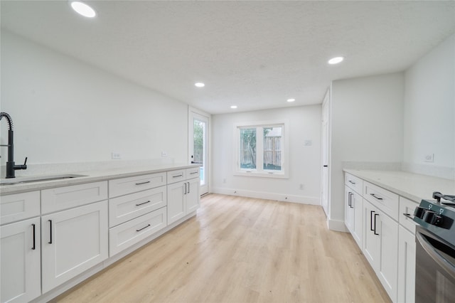 kitchen with light wood-style floors, recessed lighting, white cabinetry, a sink, and range