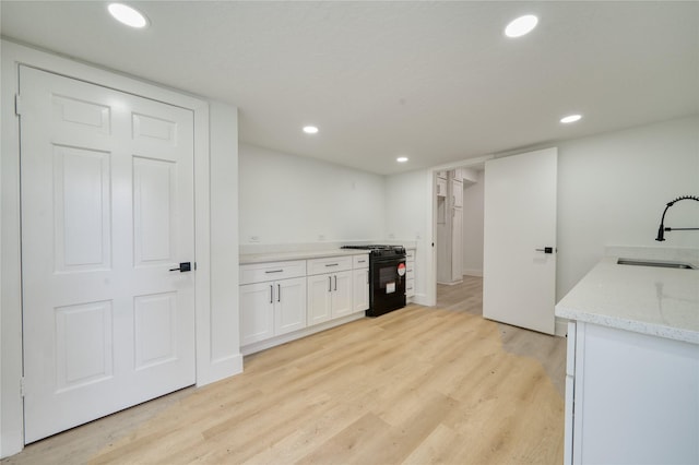 kitchen with gas stove, light stone counters, a sink, light wood-style floors, and white cabinetry