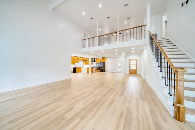 unfurnished living room with light wood-style floors, high vaulted ceiling, stairway, and beamed ceiling