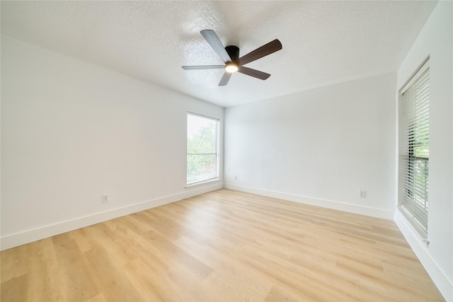 spare room featuring baseboards, a ceiling fan, light wood-style flooring, and a textured ceiling