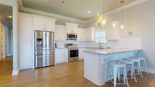 975 S Stingaree, Crystal Beach, TX 77650 - kitchen with appliances with stainless steel finishes, a peninsula, white cabinetry, light wood-type flooring, and a kitchen breakfast bar