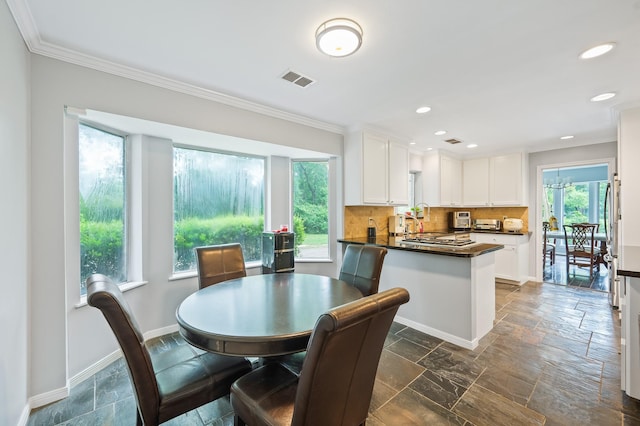dining area with stone tile floors, crown molding, visible vents, and baseboards