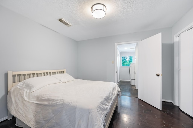 bedroom with a textured ceiling, visible vents, dark wood-style floors, and baseboards