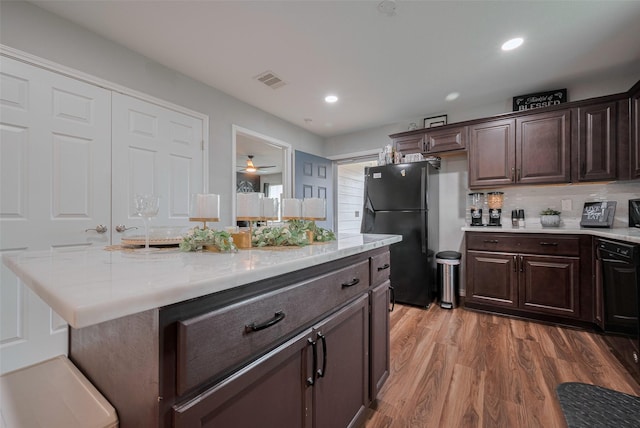 kitchen with dark brown cabinetry, light countertops, freestanding refrigerator, wood finished floors, and visible vents