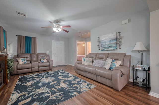 living area with ceiling fan, a fireplace, wood finished floors, and visible vents