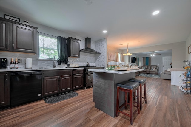 kitchen with wall chimney range hood, a breakfast bar, a sink, dishwasher, and open floor plan