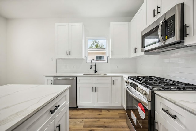 kitchen featuring appliances with stainless steel finishes, tasteful backsplash, a sink, and light wood-style floors