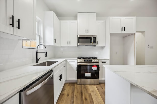 kitchen with a sink, light stone counters, white cabinets, and stainless steel appliances