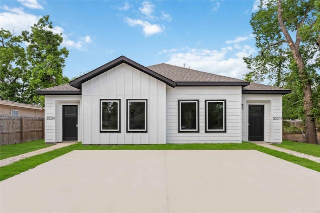 exterior space featuring fence, a shingled roof, board and batten siding, a lawn, and a patio