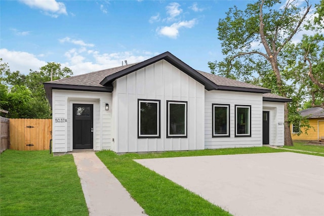 modern farmhouse with board and batten siding, roof with shingles, fence, and a front yard