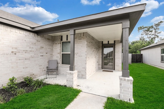 entrance to property featuring brick siding, fence, and a yard