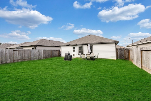 rear view of property featuring a yard, a shingled roof, and a fenced backyard