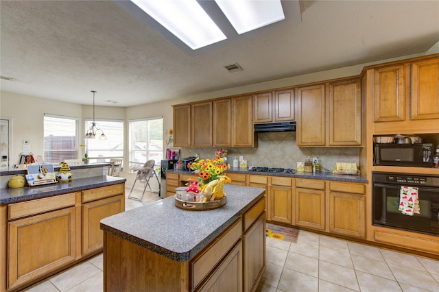 kitchen featuring dark countertops, under cabinet range hood, visible vents, a kitchen island, and black appliances