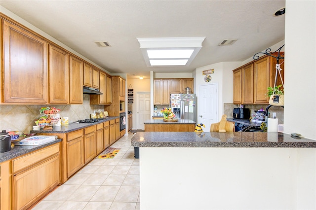 kitchen with oven, stainless steel fridge, backsplash, under cabinet range hood, and visible vents
