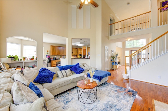 living room with a healthy amount of sunlight, stairway, light wood finished floors, and a towering ceiling